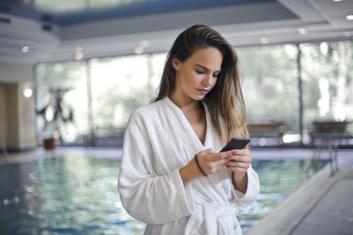 女人在使用她的智能手机时站在白色长袍池畔的选择性焦点照片 · 免费素材图片