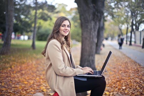 在公园中使用上网本的快乐自信的女人 · 免费素材图片