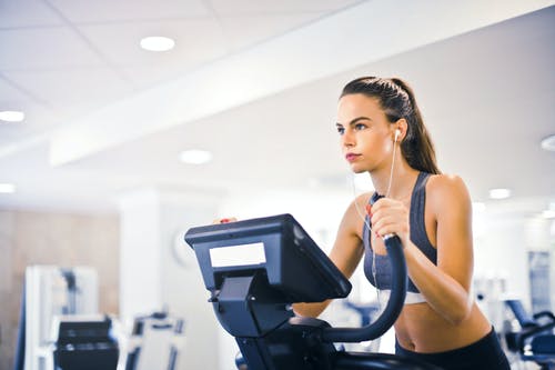 独自在现代健身房的跑步机上训练的年轻女运动员 · 免费素材图片