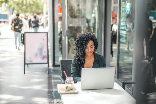 族裔的年轻女子，在现代的街头咖啡馆喝美味的饮料时使用笔记本电脑 · 免费素材图片