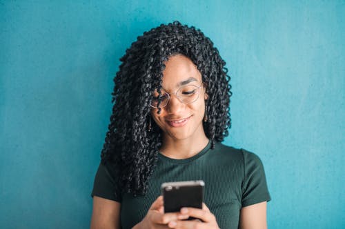 微笑的女人，穿着黑色t恤和眼镜使用她的智能手机的肖像照片 · 免费素材图片