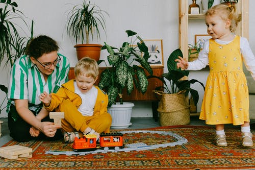 母亲和两个兄弟姐妹在家里玩玩具火车 · 免费素材图片