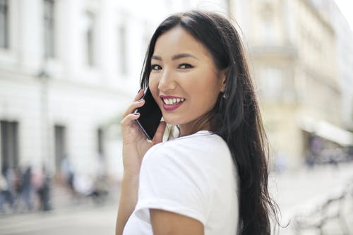 微笑的女人，穿着白色t恤通电话的选择性焦点照片 · 免费素材图片