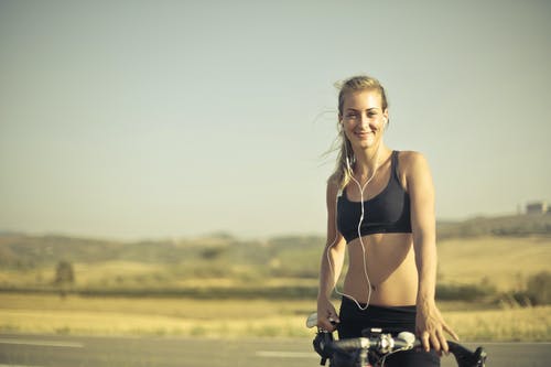 黑色主动穿带耳机站在路边她的自行车旁边的耳机的微笑妇女的选择性聚焦照片 · 免费素材图片