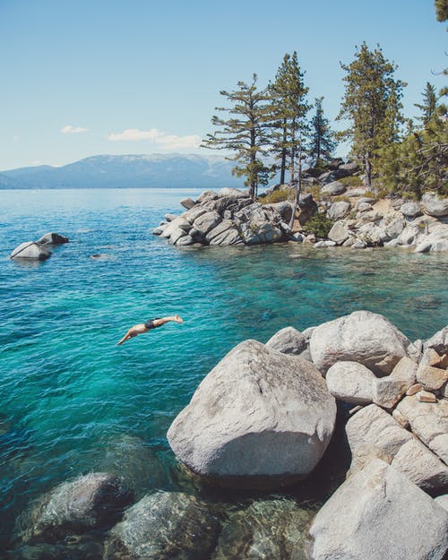 平静的湖面，在岩石地形与游客跳入水中 · 免费素材图片