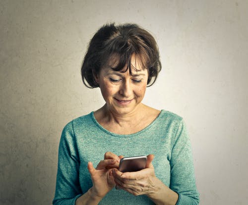 绿色长袖衬衫的老妇正在使用智能手机很开心 · 免费素材图片