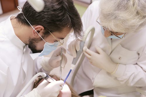 牙医和护士在女人的牙齿上工作 · 免费素材图片