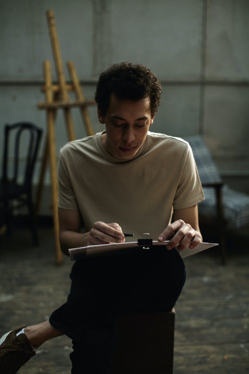 一个男人坐在木椅上素描在白色纸板上 · 免费素材图片