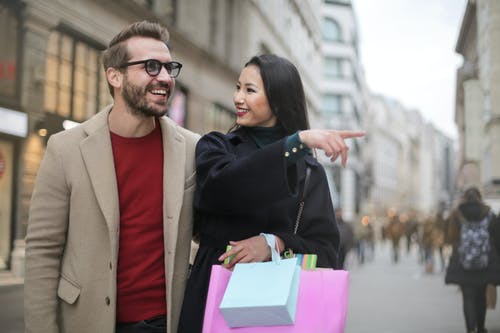 快乐的多种族成人夫妇与沿着市中心的街道上行走的购物袋 · 免费素材图片