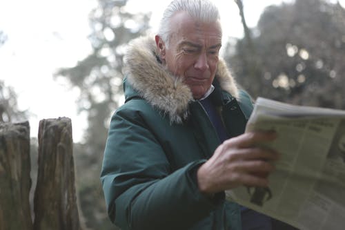穿着绿色大衣的男人阅读新闻纸 · 免费素材图片