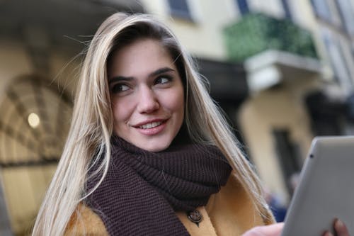 女人穿着棕色外套和栗色的围巾，拿着ipod · 免费素材图片