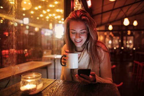 女人抱着看着她的手机的白色陶瓷杯 · 免费素材图片