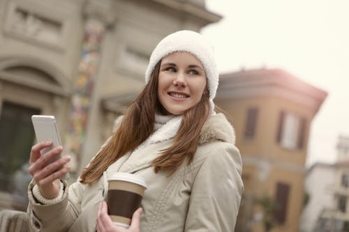 拿着棕色和白色一次性杯子的白色编织帽的女人 · 免费素材图片