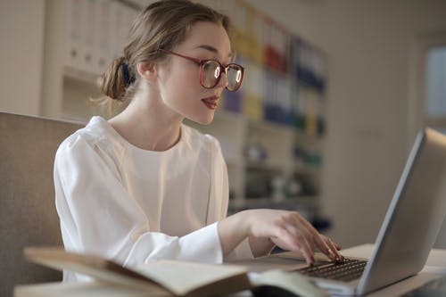 使用一台笔记本电脑的白色长袖衬衫的女人 · 免费素材图片