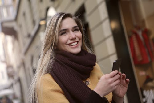 拿着智能手机的棕色围巾的女人 · 免费素材图片