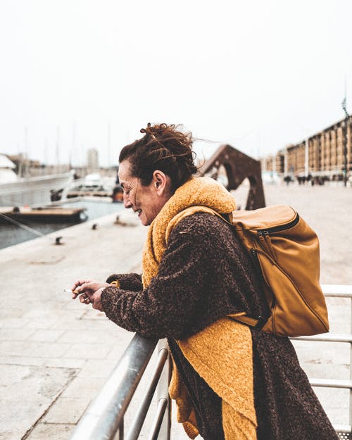 棕色外套斜倚在金属扶手上的女人 · 免费素材图片