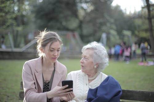 教资深母亲的成年女儿在公园使用智能手机 · 免费素材图片