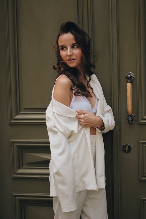白色意大利面条皮带礼服站在棕色的木门旁边的女人 · 免费素材图片