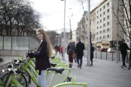 紫大衣站在绿色的自行车上的女人 · 免费素材图片