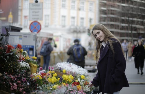 紫罗兰色外套站在鲜花旁的女人 · 免费素材图片