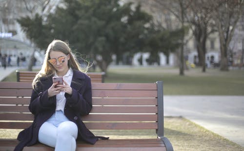 女人坐在板凳上使用手机 · 免费素材图片