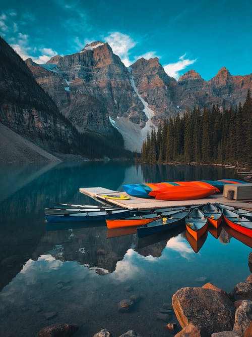 棕色和白色的小船，在树木和山附近的湖上 · 免费素材图片