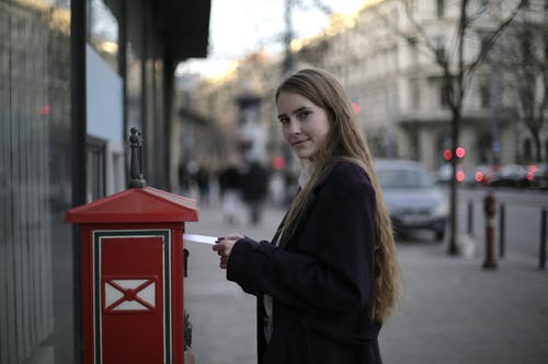站在邮箱旁边时穿紫大衣的女人 · 免费素材图片