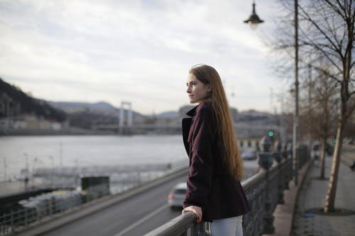 紫罗兰色外套站在金属栏杆附近的女人 · 免费素材图片