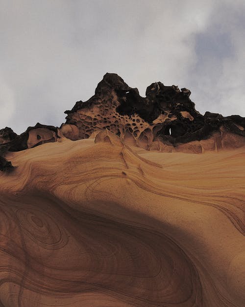 多云的天空下沙漠中的沙质地形上的岩层 · 免费素材图片