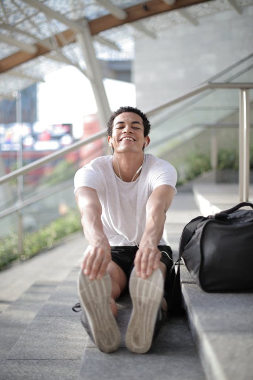 坐在楼梯上伸展的男人的照片 · 免费素材图片