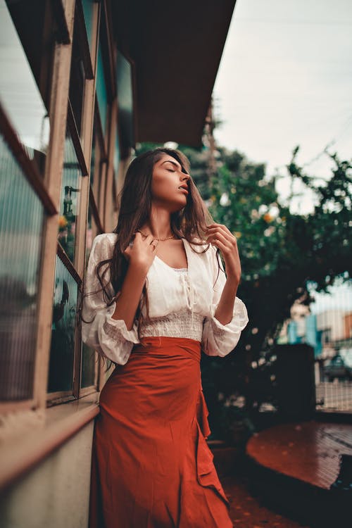 白色蕾丝长袖衬衫和红色裙子站在人行道上的女人 · 免费素材图片