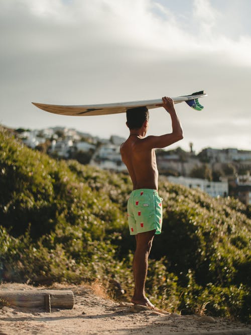 裸照穿着绿色短裤，抱着冲浪板的人 · 免费素材图片