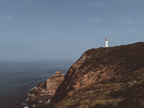 水体附近悬崖上的灯塔照片 · 免费素材图片