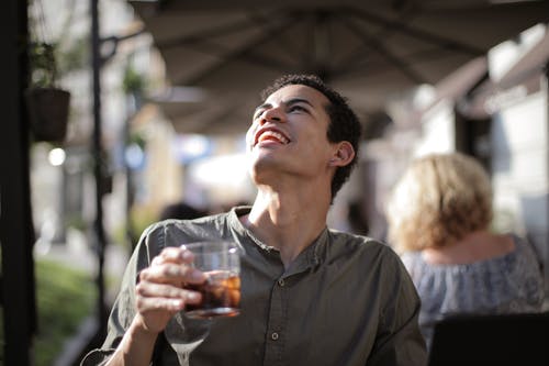 快乐的族裔男子在阳光明媚的炎热的日子在街边的咖啡馆喝与冰块的饮料 · 免费素材图片
