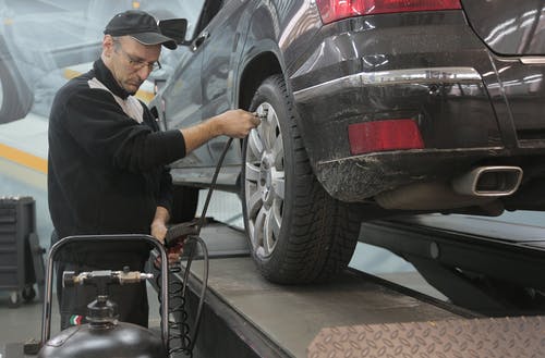 严重的汽车修理工在现代服务车库中抽气车轮 · 免费素材图片