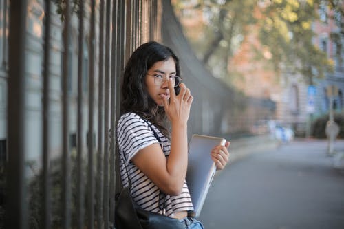 白色和黑色的条纹的衬衫和黑色外套拿着笔记本电脑的女人 · 免费素材图片