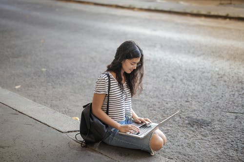 黑色和白色的条纹衬衫，坐在人行道上使用macbook Pro的女人 · 免费素材图片