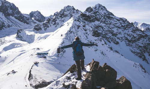 蓝色外套和黑裤子的人站立在积雪的山上 · 免费素材图片