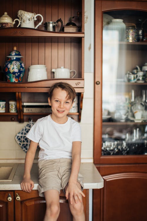 男孩微笑着坐在厨房的柜台上的照片 · 免费素材图片