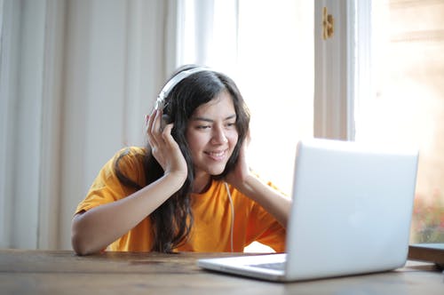 坐在桌子旁使用macbook的橙色衬衫的女人 · 免费素材图片