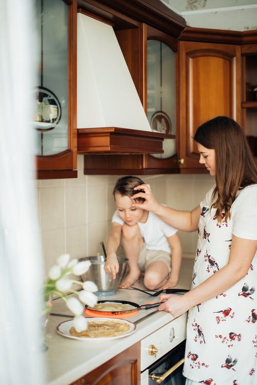 年轻的母亲带着儿子在厨房里做可丽饼 · 免费素材图片