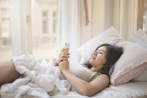在床上使用智能手机的年轻女子 · 免费素材图片