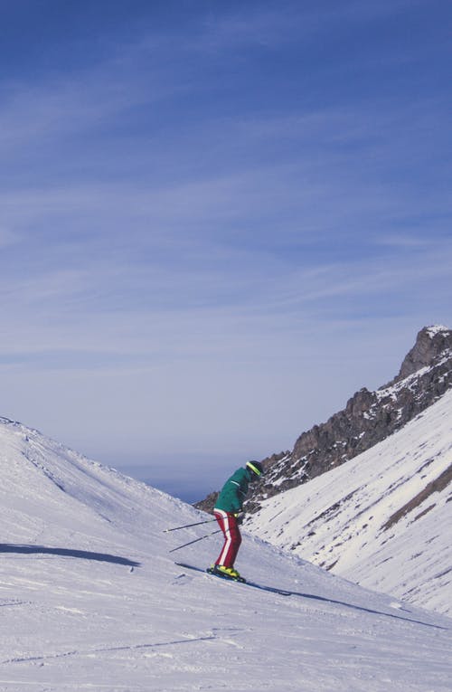 绿色外套和蓝色的裤子，站在雪覆盖的山上的人 · 免费素材图片
