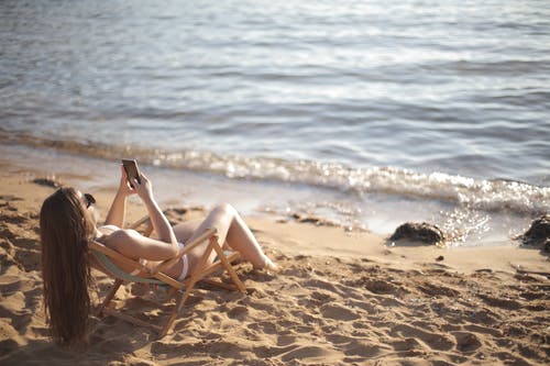 躺在海滩上的沙滩椅上的白色比基尼的女人 · 免费素材图片