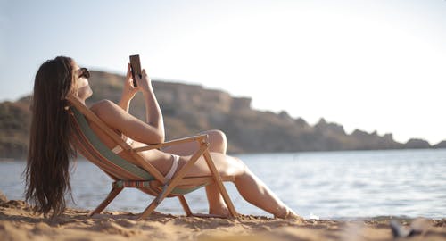 斜倚在木制折叠沙滩椅上的白色比基尼的女人 · 免费素材图片