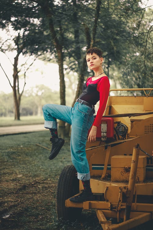 摆在黄色拖拉机上的红顶和蓝色牛仔牛仔裤的女人 · 免费素材图片