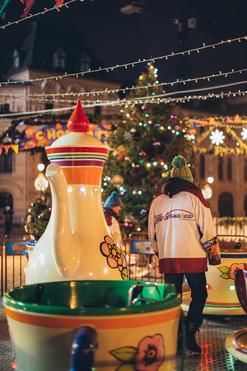 员工服务旋转木马走在巨大的茶壶和杯子在圣诞节风格装饰的夜晚公园里 · 免费素材图片