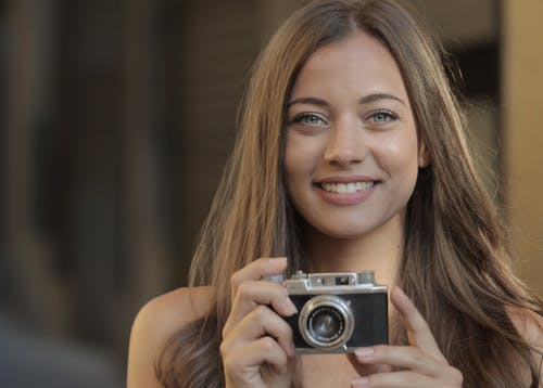微笑的女士拿着灰色和黑色的相机 · 免费素材图片