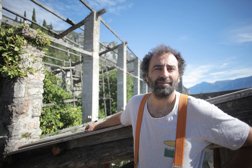 站在棕色木栅栏附近的白船员脖子t恤的男人 · 免费素材图片