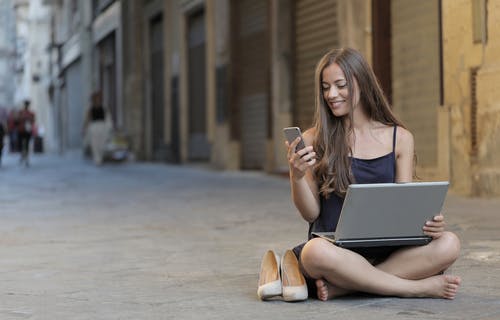 使用智能手机和笔记本电脑时坐在地板上的女人的照片 · 免费素材图片
